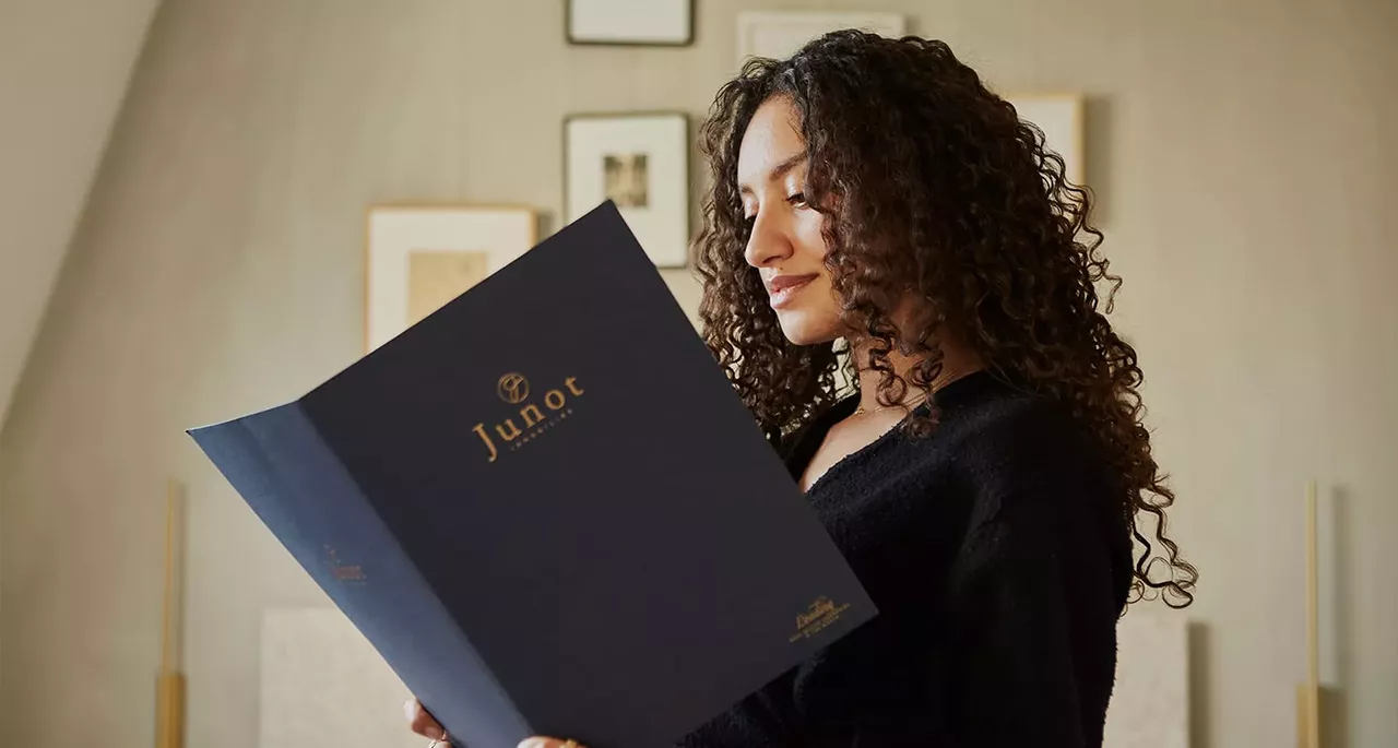 A woman with dark, curly hair holding a Junot brochure in her hands