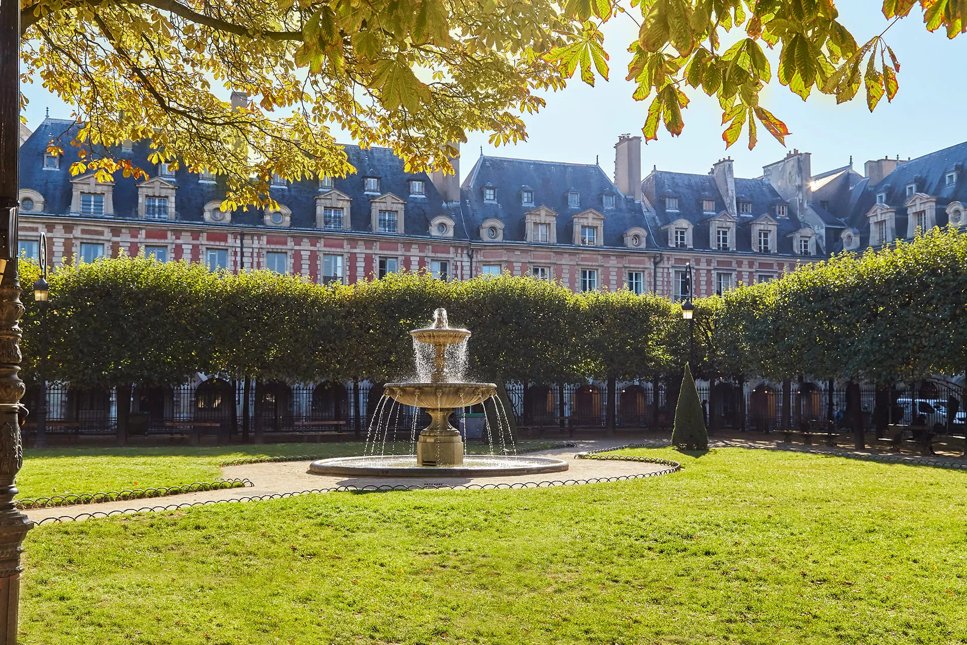 Place des Vosges dans le Marais, avec ses fontaines, jardins soignés et immeubles en briques rouges emblématiques.