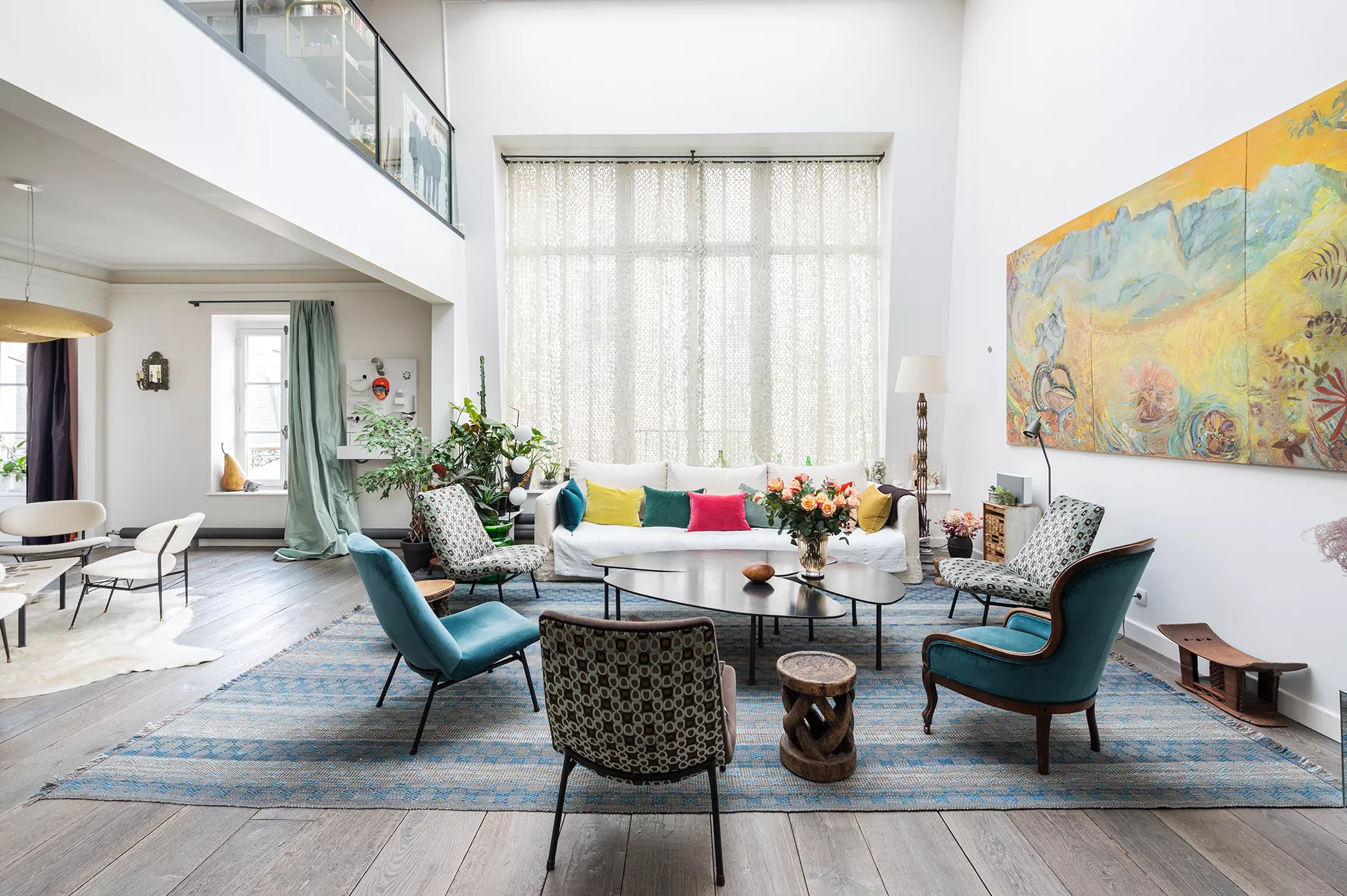 Salon lumineux d’un duplex dans le 6ᵉ arrondissement de Paris, décoré avec soin, avec de grands rideaux filtrant une lumière douce.